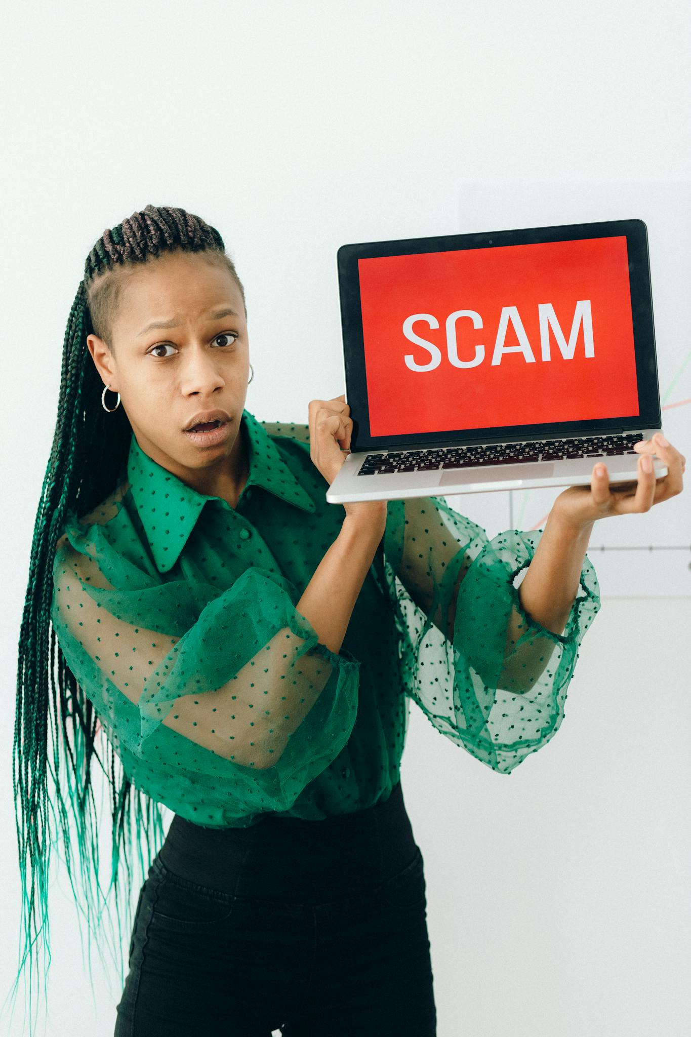 A shocked woman holding a laptop displaying a scam alert in a bright room.
